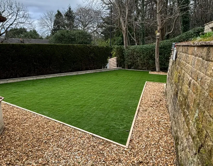 Large artificial lawn with crisp edging and gravel borders beside a mature stone wall
