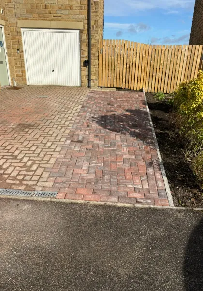 Block paved driveway extension laid beside a stone garage and timber gate