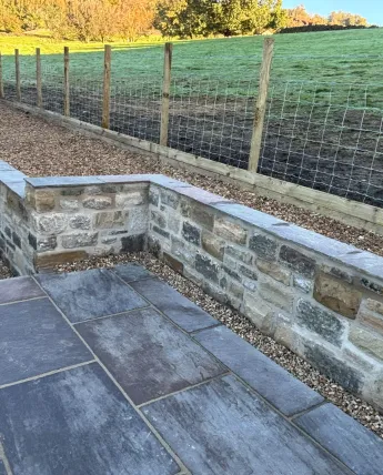New natural stone retaining wall with dressed coping stones beside a country garden