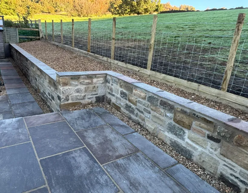 New natural stone retaining wall with dressed coping stones beside a country garden