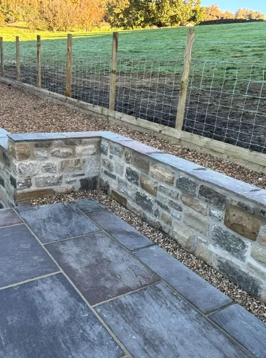 New natural stone retaining wall with dressed coping stones beside a country garden