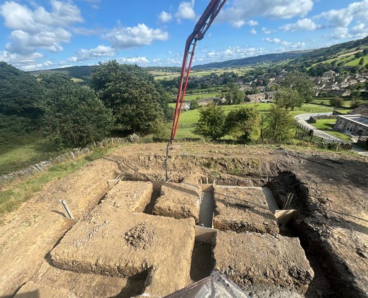 Concrete being pumped into foundation trenches on a hillside groundworks site overlooking a Yorkshire valley