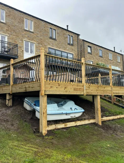 Large raised timber deck with decorative railings built into a steep riverside garden