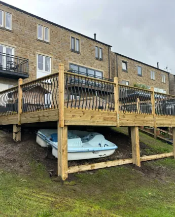 Raised timber deck with decorative metal railings built on a riverside garden slope