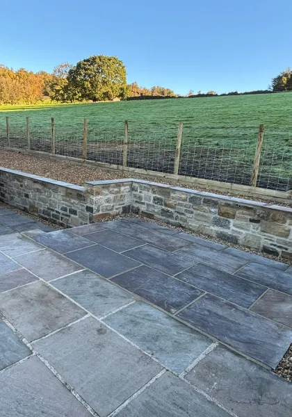 Finished slate patio with matching paths and a capped natural stone retaining wall