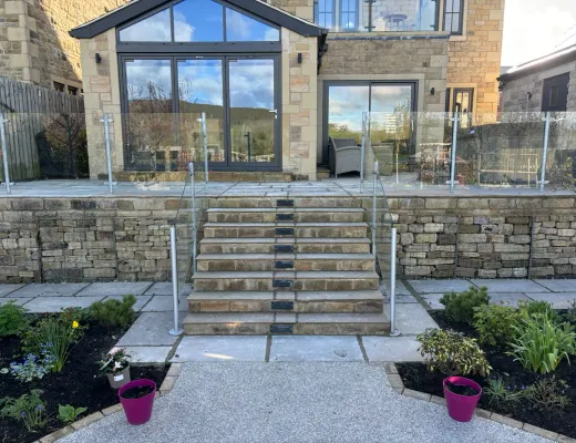 Wide stone garden steps with glass balustrades, planted borders and a raised terrace