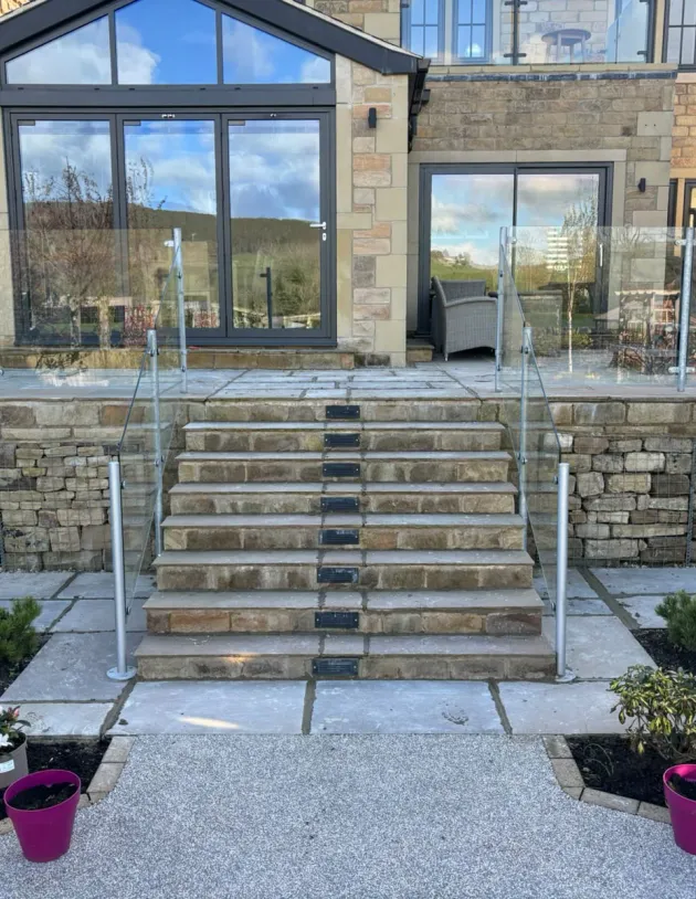 Wide stone garden steps with glass balustrades, planted borders and a raised terrace