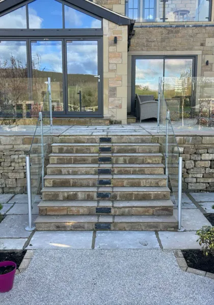 Wide stone garden steps with glass balustrades, planted borders and a raised terrace